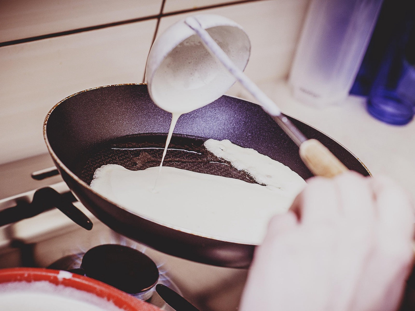 Pancake batter being poured into a nonstick frying pan on a gas stove